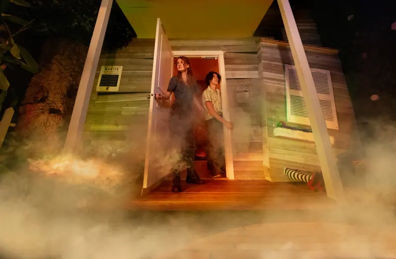 Two players hold a farmhouse door open in the fog on the Journey to Oz set